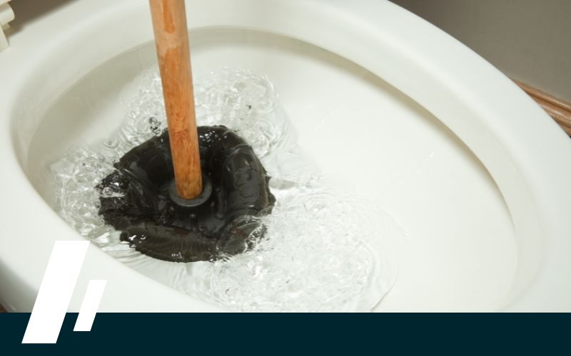 Issaquah Sewer Line Replacement 1 - Dirt Cheap Sewer Co. Wooden-handled plunger in a clogged white toilet bowl with water swirling around the rubber suction head.
